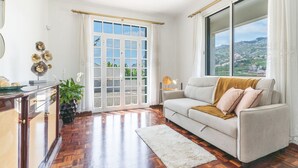 A spacious living room with a large window, a sofa, a coffee table, and a potted plant. - Casa do Pico by Atlantic Holiday (Camara de Lobos)