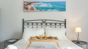 A neatly made bed with a tray of croissants and juice, a bedside lamp, and a painting of a coastal scene. - Casa do Pico by Atlantic Holiday (Camara de Lobos)