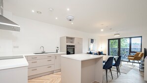 A modern kitchen with a central island, built-in appliances, and a dining area with chairs and a table. - Whispers in Light 65s Stay (Surrey)