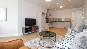 A modern living room with a sofa, a glass coffee table, and a TV. - Quiet Luxe Escape 65s Only (Surrey)