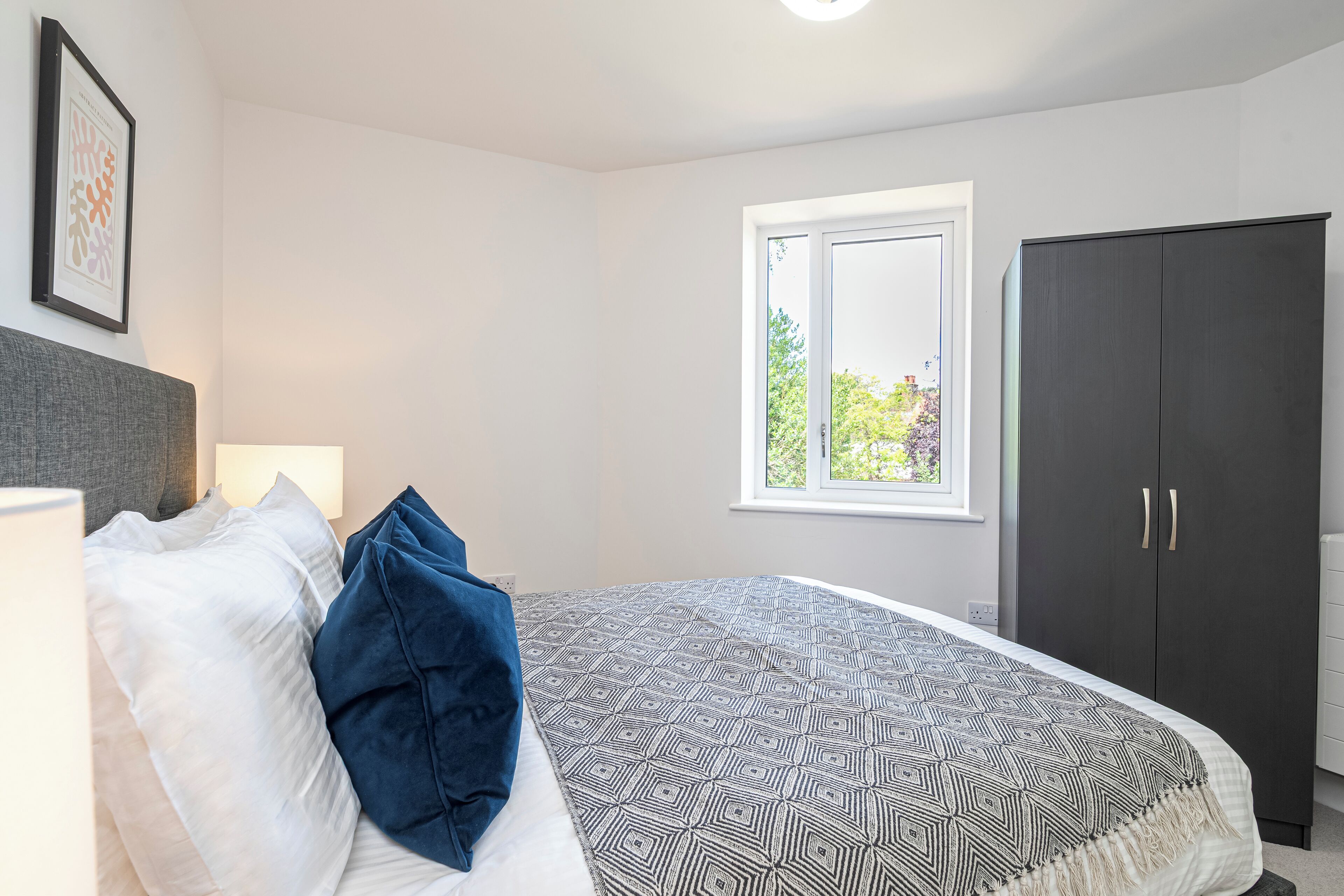 Een slaapkamer met een bed, een kledingkast, een raam en een ingelijste foto aan de muur.
