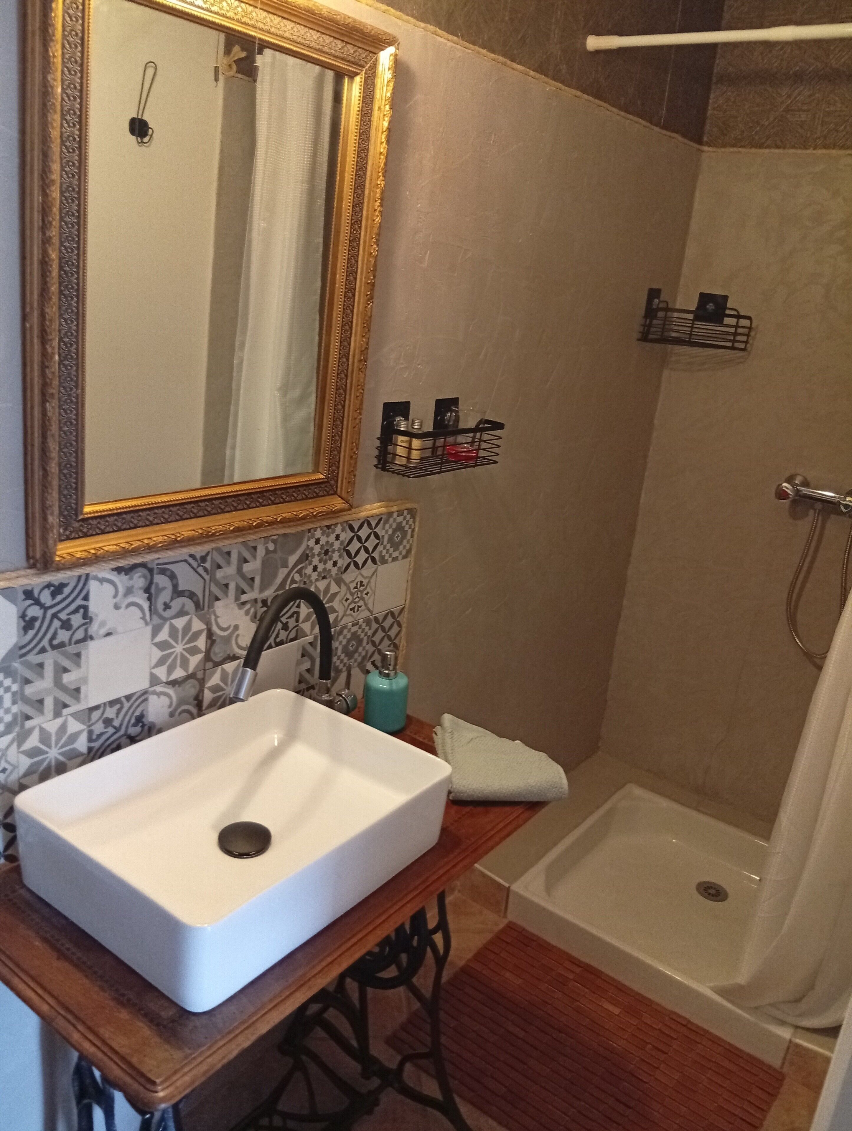 A bathroom with a white sink, a mirror with a gold frame, a shower, and a towel on the counter.