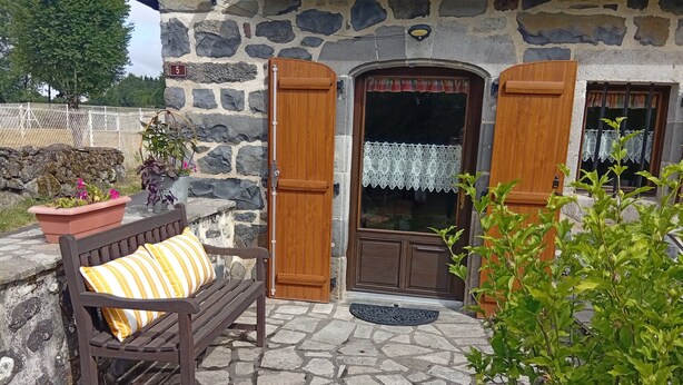 A stone building with a wooden bench, a potted plant, and a door with a lace curtain.