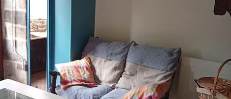 Una habitación acogedora con una mesa de vidrio que exhibe caracoles, un sofá azul con cojines estampados y una cesta de mimbre sobre un taburete azul.
