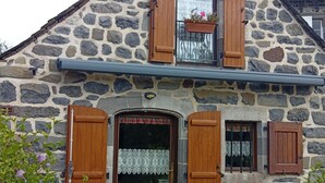 A stone building with wooden shutters, a front door, and a small table with a bench.