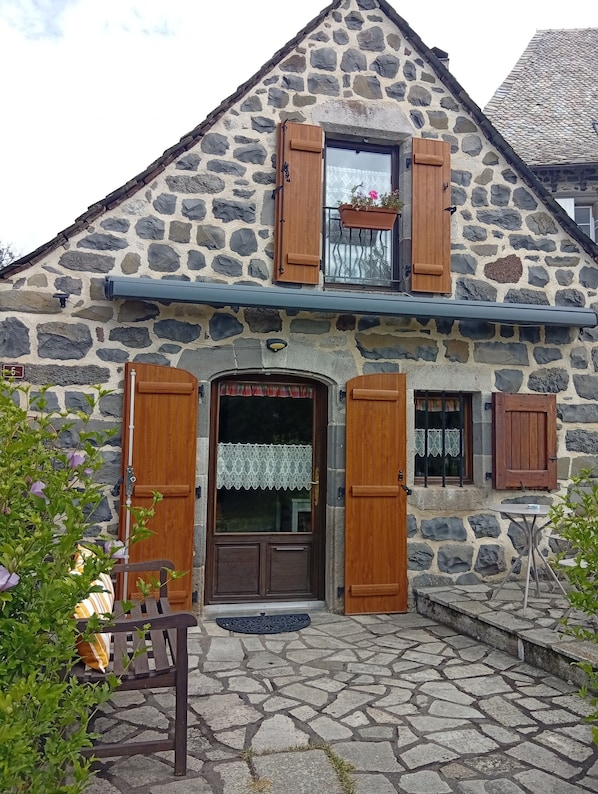 Un bâtiment en pierre avec des volets en bois, une porte d’entrée et une petite table avec un banc.