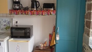 A compact kitchen with a microwave, coffee maker, and kettle on the countertop, a small refrigerator, and a teal door.