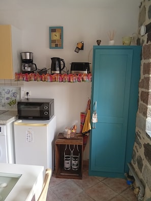 Une cuisine compacte équipée d’un four à micro-ondes, d’une machine à café et d’une bouilloire sur le plan de travail, d’un petit réfrigérateur et d’une porte de couleur turquoise.