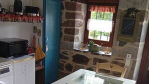A kitchen with a stone wall, a blue cabinet, a microwave, a kettle, and a glass display case with food items.