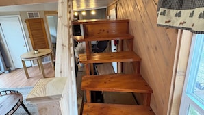 A wooden staircase with a railing, leading to a second-floor area with a window and a door. - Awesome Cabin right off US 160 (Bayfield)