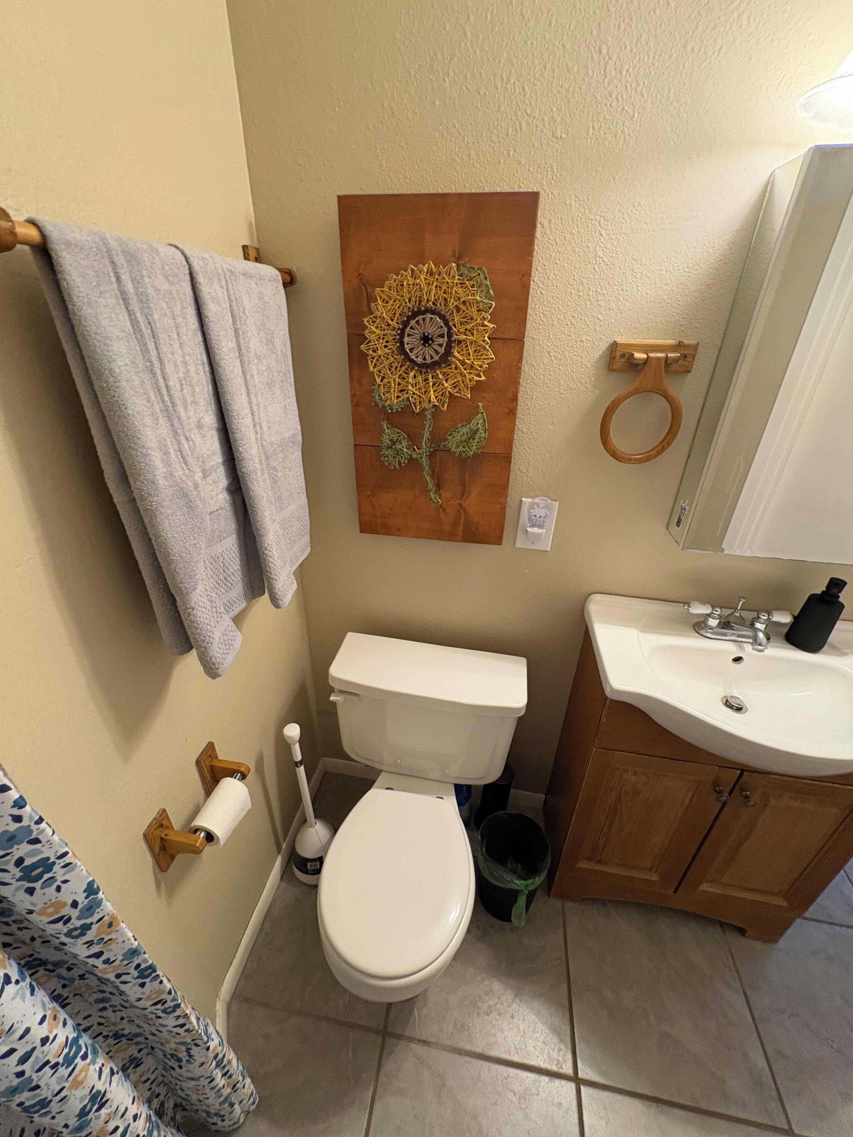 A bathroom with a toilet, sink, and a wall-mounted artwork of a sunflower.