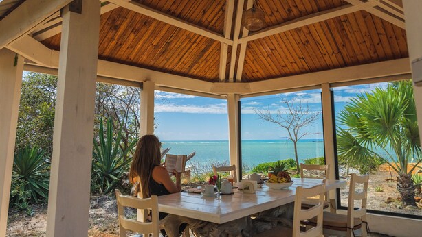 Un espace extérieur abrité, avec vue sur l’océan, des poutres en bois et une table entourée de chaises.