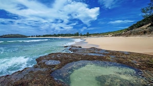 Une plage à l’eau claire, avec un rivage rocheux et une île visible au loin.