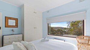 Ein Schlafzimmer mit Bett, Schminktisch, Fenster mit Blick und einem Korbstuhl.