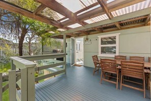 A covered outdoor area with a wooden deck, a table with chairs, and a door labeled 'At the Beach.' - Salt Shack | Beachfront Retro Escape + Pets (Guerilla Bay)