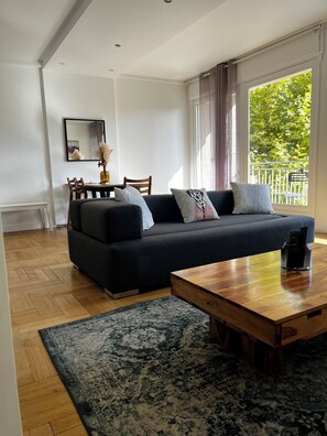 A modern living room with a dark sofa, a wooden coffee table, and a dining area with chairs and a table.