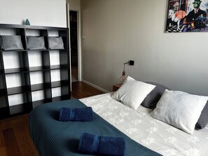 A bedroom with a bed, pillows, a wall-mounted shelf, and a painting.