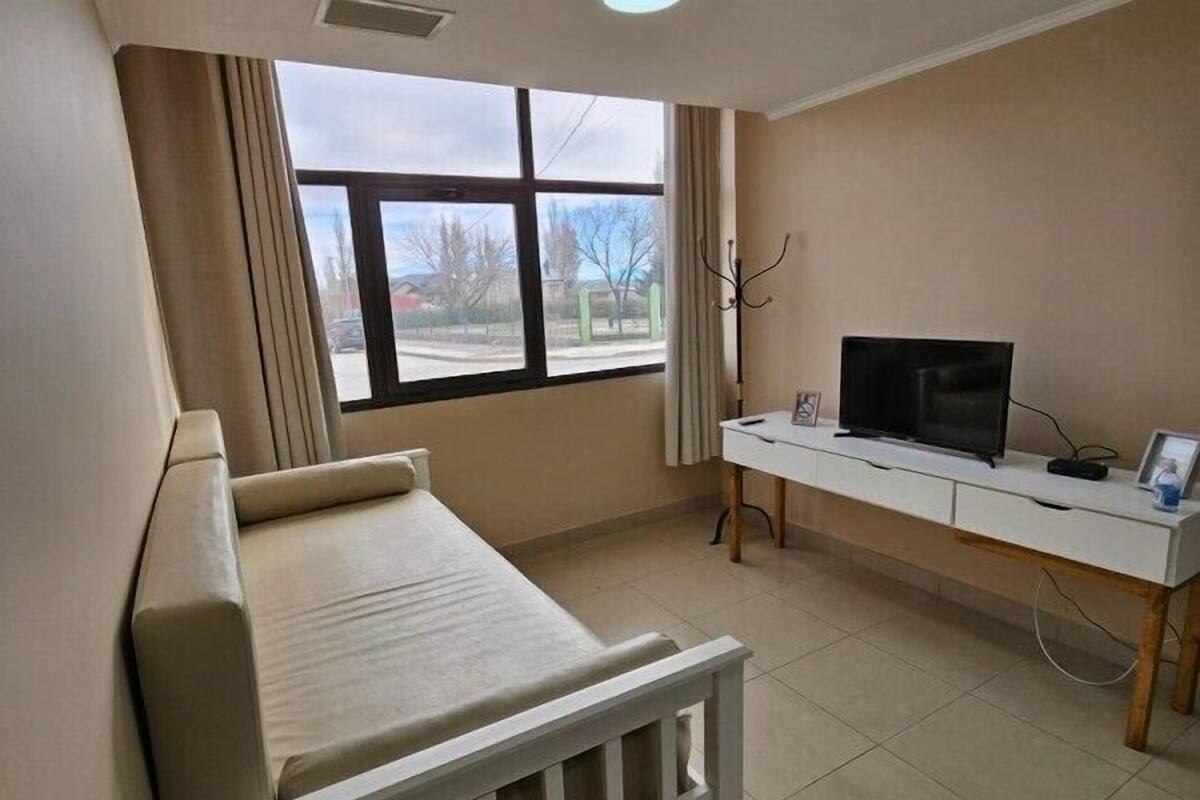 Ein Zimmer mit einem Bett, einem Schreibtisch mit Fernseher und einem Fenster mit Vorhängen.