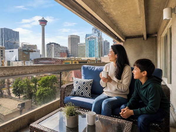 A balcony with a city view, a sofa, a table with a plant, and a mug.