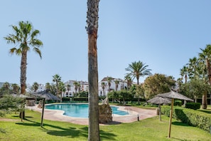 A pool surrounded by palm trees and a building with a white facade in the background.