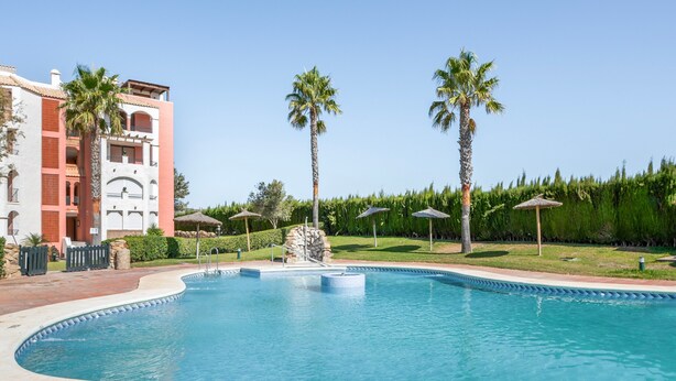 A swimming pool with a curved edge, surrounded by palm trees and a building with balconies. - Apartment 'Vistas Al Mar' with Sea View, Private Pool and Wi-Fi (Tarifa)