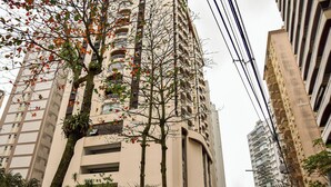 A tall building with multiple balconies and a tree in front. - Flat com Piscina e Lazer na Praia de Pitangueiras (Guarujá)