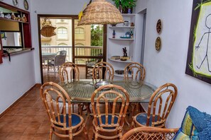 A dining area with wicker chairs and a glass table, a wicker hanging light, and a balcony with a view. - Flat com Piscina e Lazer na Praia de Pitangueiras (Guarujá)