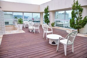 A rooftop terrace with wooden flooring, white plastic chairs, and tables. - Flat com Piscina e Lazer na Praia de Pitangueiras (Guarujá)