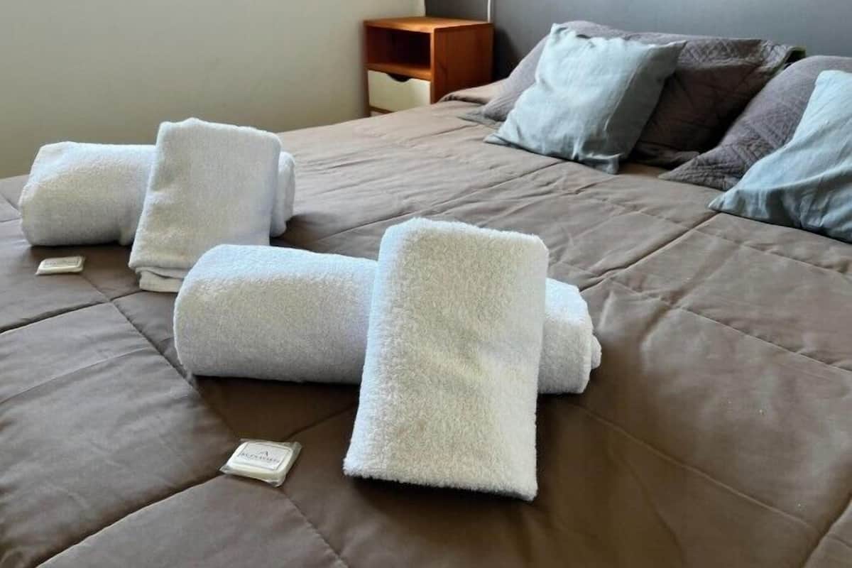 Un letto rifatto con asciugamani bianchi arrotolati e un comodino in legno accanto.