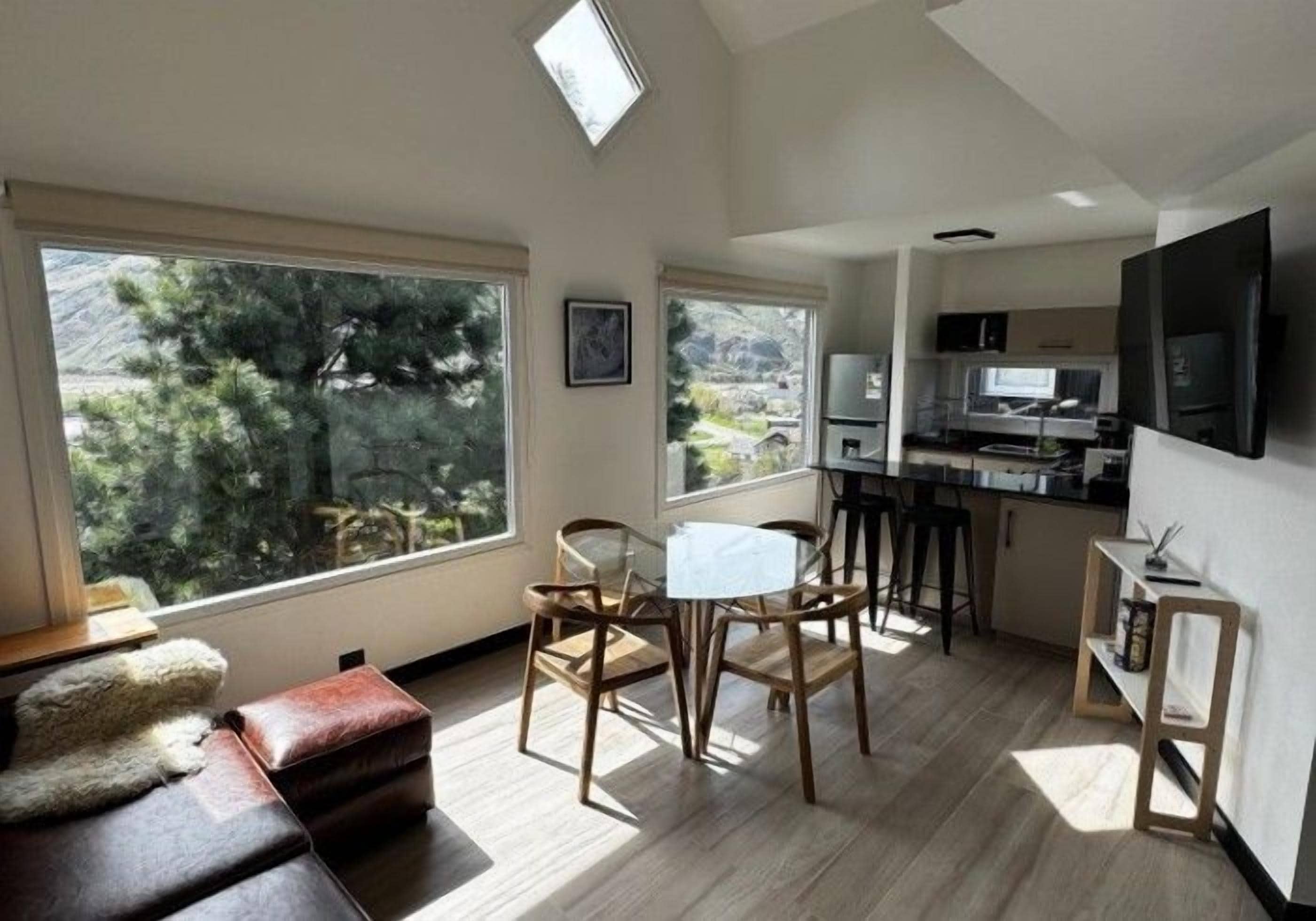 Una sala de estar moderna con un ventanal grande, una zona de comedor y una cocina con televisor de pantalla plana.