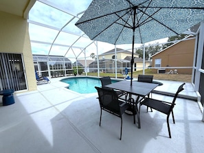 A covered outdoor area with a pool, a table with chairs, and a view of a residential neighborhood. - Beautiful South-facing Pool Home in Southern Dunes (Haines City)