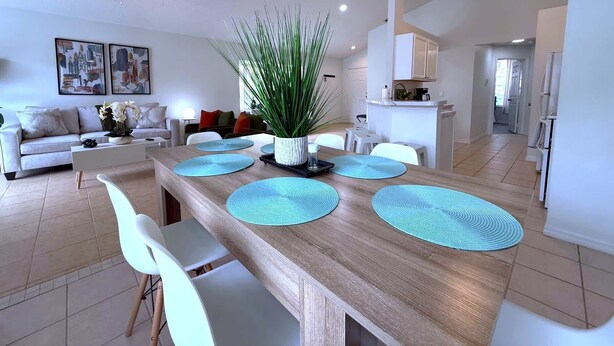 Un coin repas moderne avec une table en bois, des chaises blanches et des sets de table bleus.