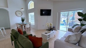 Un salon moderne comprenant un canapé, des fauteuils, un coin repas et un téléviseur.