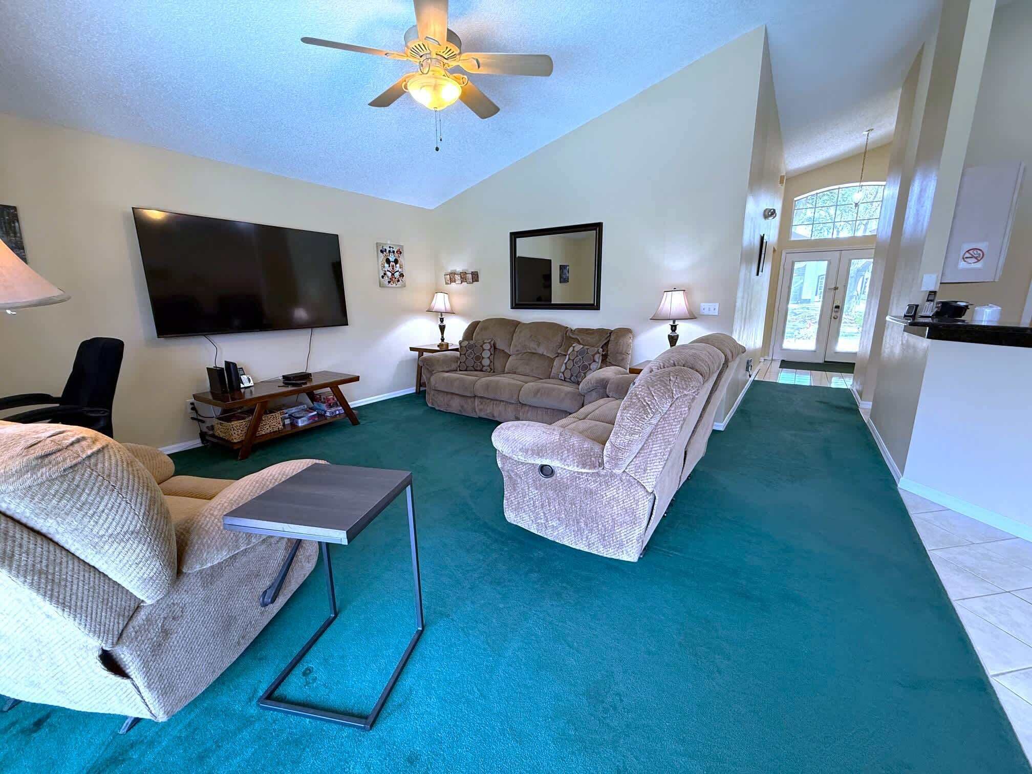 A living room with a flat-screen TV, two sofas, a coffee table, and a ceiling fan.