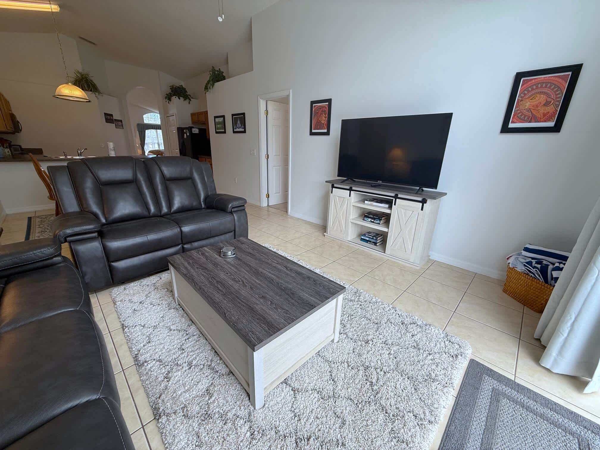 A modern living room with a black leather sofa, a wooden coffee table, and a flat-screen TV on a wooden stand.