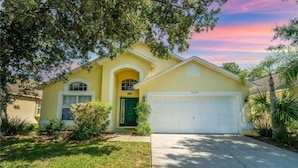 A yellow house with a green door, a garage, and a driveway. - 4 Bedroom Villa With Private Pool & Golf Course Views (Haines City)