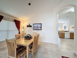 A dining area with a wooden table and chairs, a pendant light, and a framed picture on the wall.
