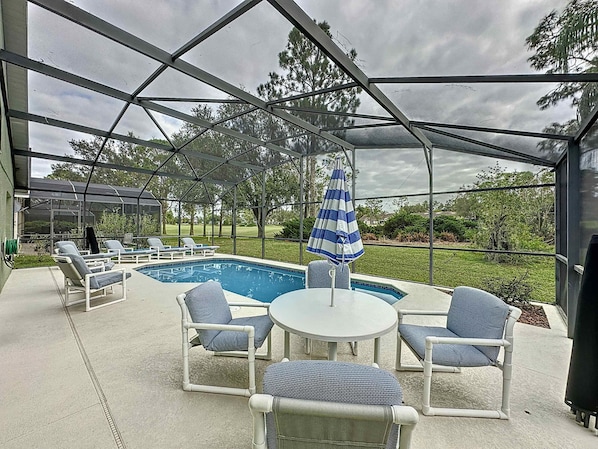 A covered outdoor area with a pool, lounge chairs, and a table.