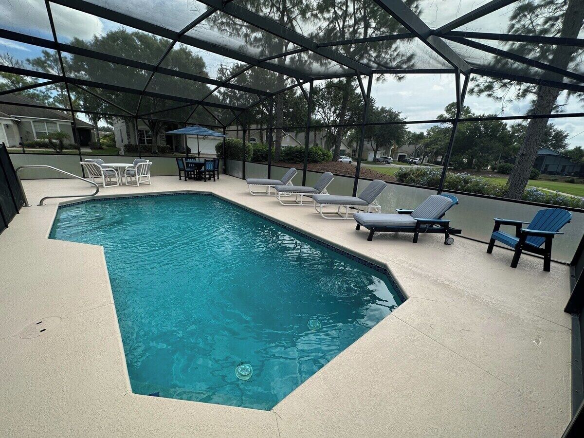 A swimming pool with a curved edge, surrounded by lounge chairs and a covered patio area.