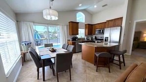A modern kitchen with a central island, dining area with chairs, and a view of a swimming pool. - South Facing Updated Southern Dunes Villa (Haines City)