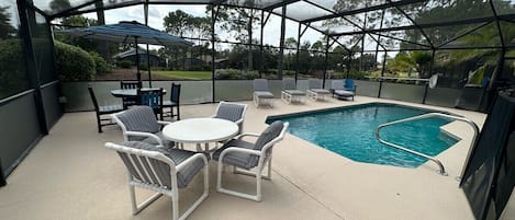 A covered outdoor area with a pool, lounge chairs, and a table.