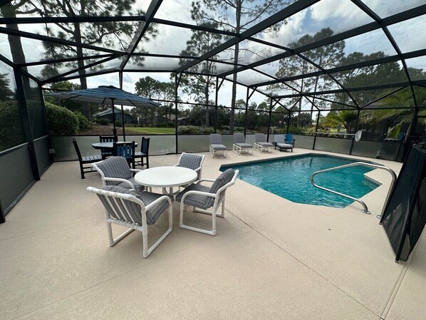 A covered outdoor area with a pool, lounge chairs, and a table.