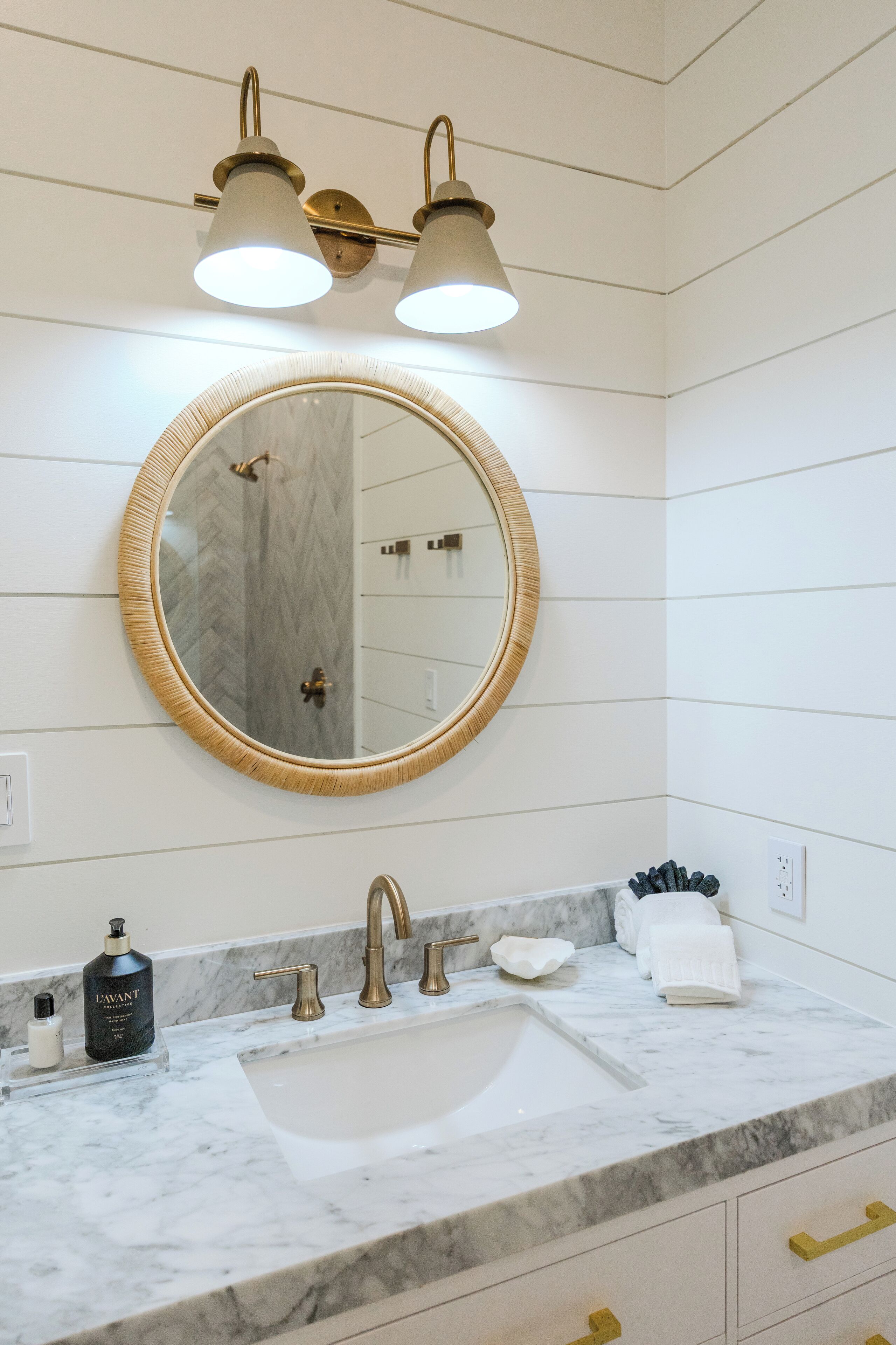 Une salle de bain avec un lavabo en marbre blanc, des robinetteries dorées et un miroir rond doté d’un cadre doré.