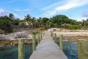 A wooden pier leading to a beach with palm trees and a clear sky.