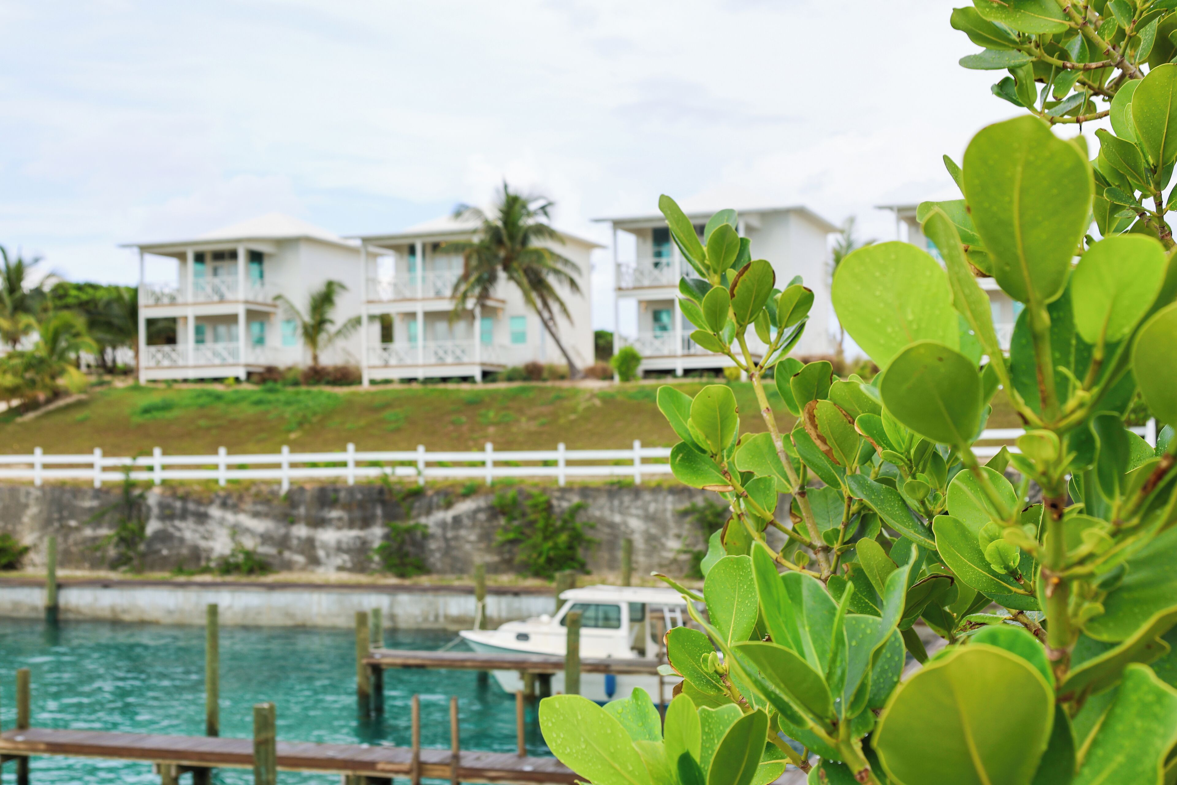 A coastal hotel with a white fence, a dock, and a boat.