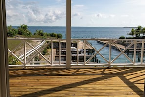 A wooden deck with a white railing overlooking a marina with boats and a distant shoreline.