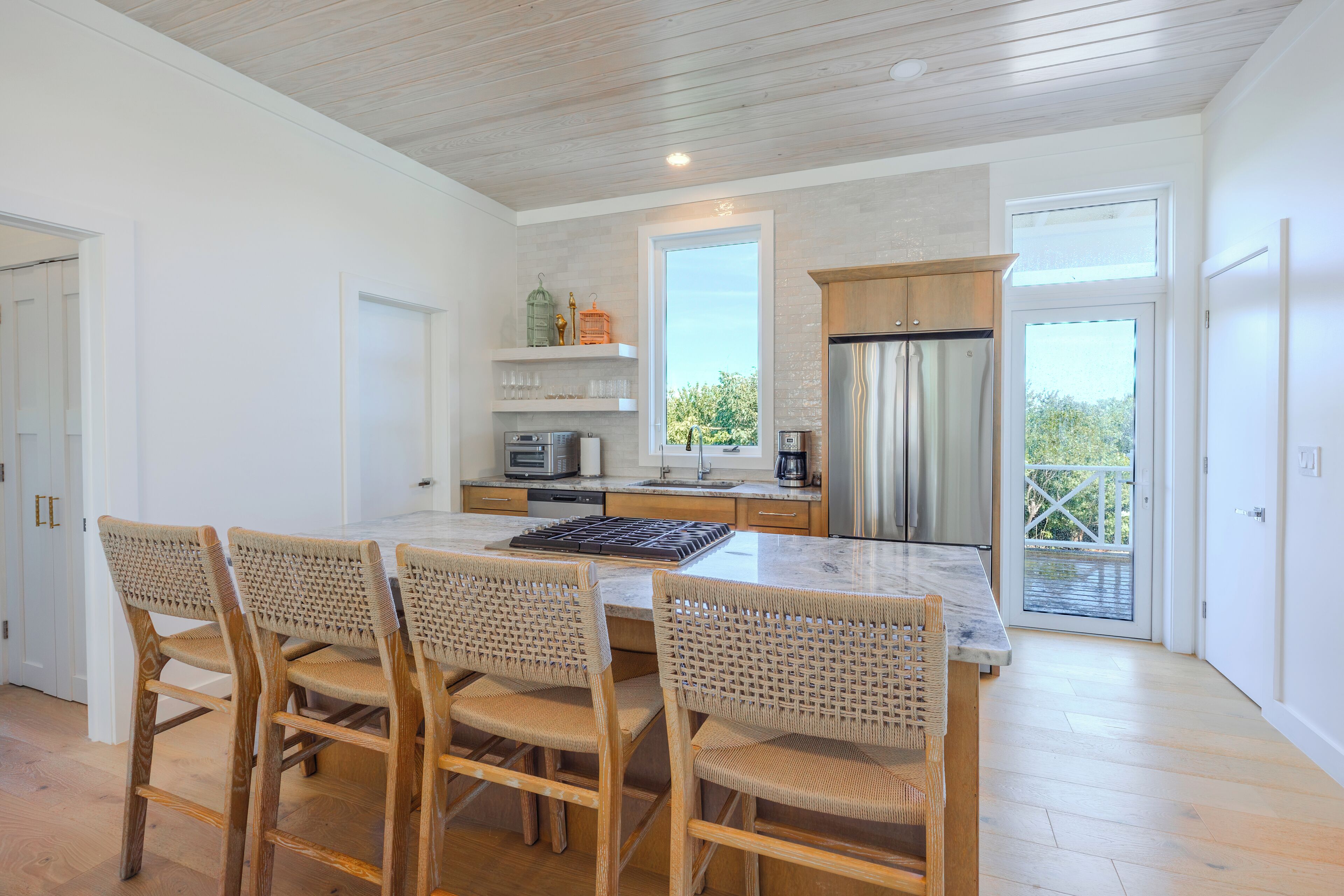 A modern kitchen with a large island, wooden chairs, and a view of the outdoors.