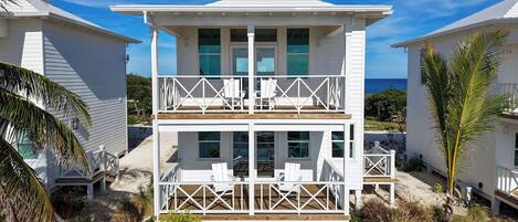 Ein Strandhaus mit zwei Etagen, einem Balkon und einer Sitzgelegenheit im Freien.