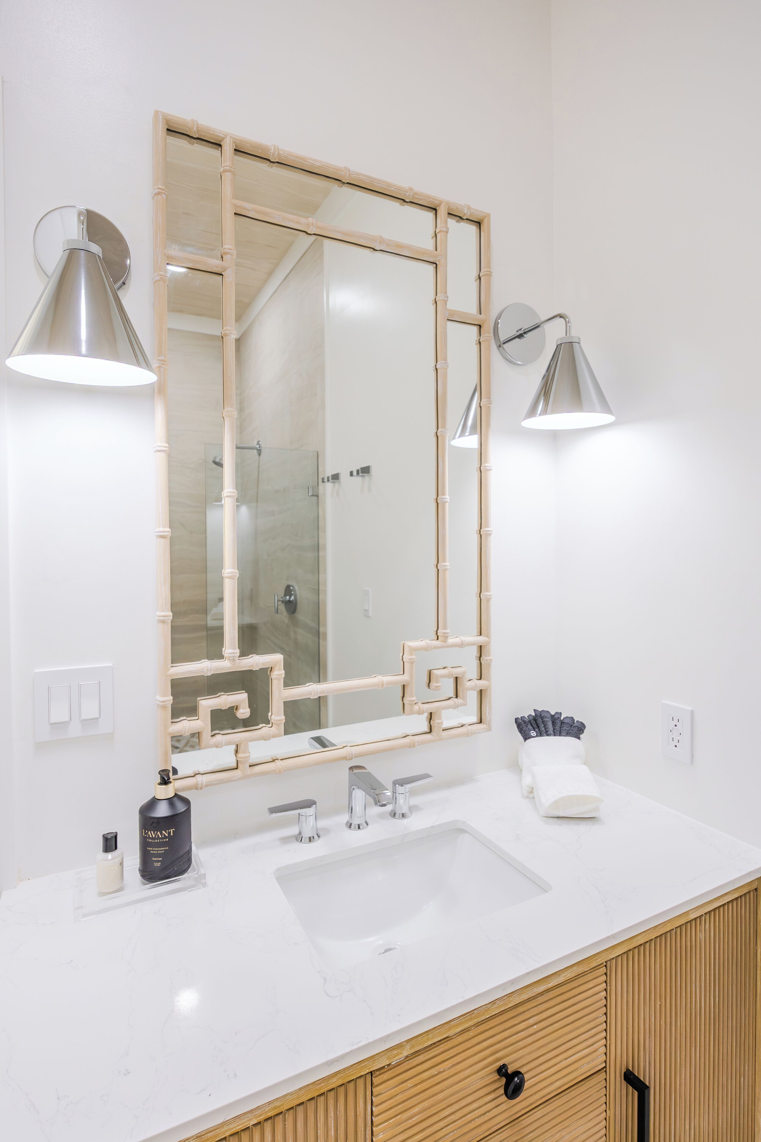 A bathroom with a large mirror, two wall-mounted lights, a sink, and a wooden cabinet.
