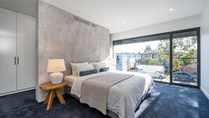 Une chambre moderne avec un grand lit, une table de chevet avec une lampe et une vue sur l’extérieur grâce à une grande fenêtre.